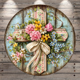 A round wooden cross adorned with a vibrant floral arrangement, including pink roses, yellow flowers, and blue flowers, is displayed against a weathered wooden background.