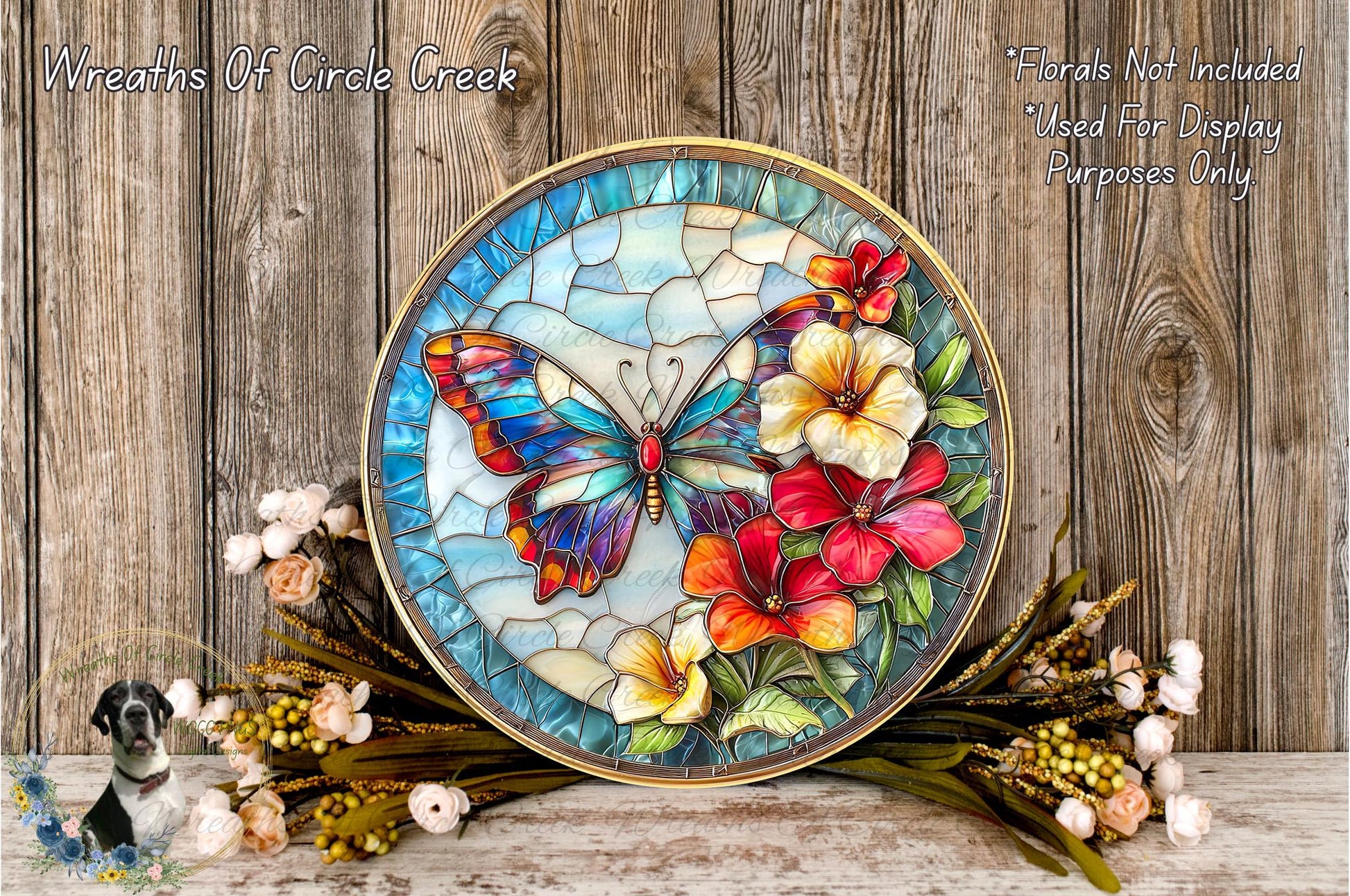 A decorative glass butterfly with colorful flowers is displayed on a wooden surface, surrounded by flowers and greenery.