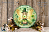 A round, decorative plate featuring a fairy with a green hat and green dress, surrounded by flowers and greenery, against a wooden background.