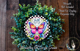 A wreath made of green leaves and flowers, with a colorful butterfly design in the center. The wreath is surrounded by a wooden background.