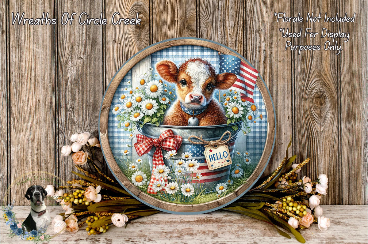 A decorative plate featuring a cow surrounded by flowers and an American flag, with the word "Hello" written on it. The plate is placed on a wooden surface, and there are flowers and a bird in the background.