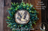 A wreath made of green foliage and a wooden frame, featuring a detailed illustration of a bird in flight.