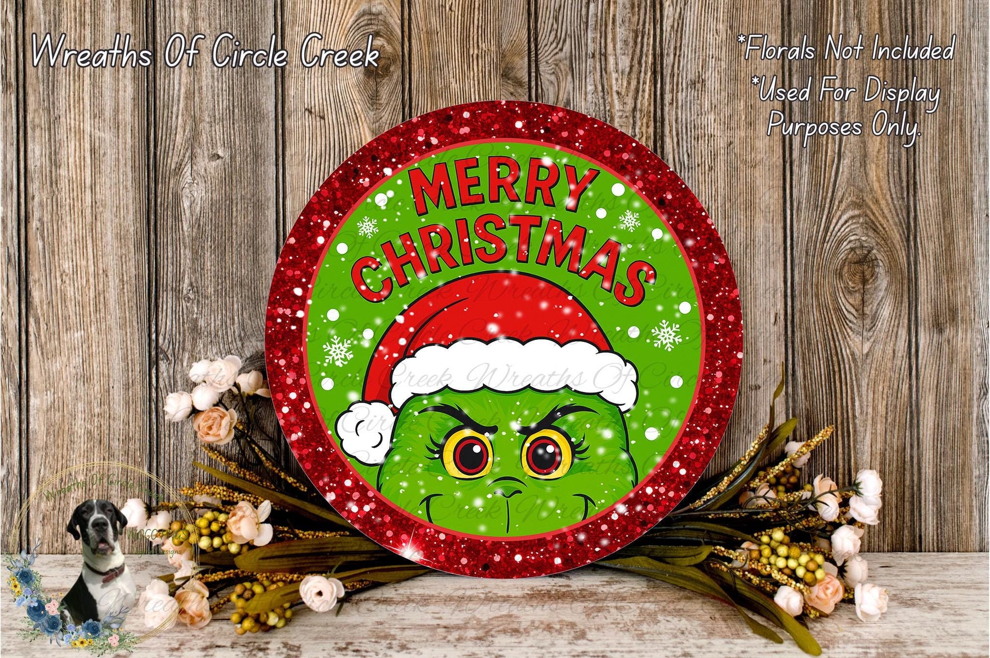 A festive Christmas wreath with a green Grinch wearing a Santa hat, surrounded by flowers and a wooden background.