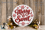 a festive wreath with the text "Merry & Sweet" written on it, surrounded by red and white candy canes and flowers. The wreath is displayed on a wooden surface, and there is a small dog in the background.