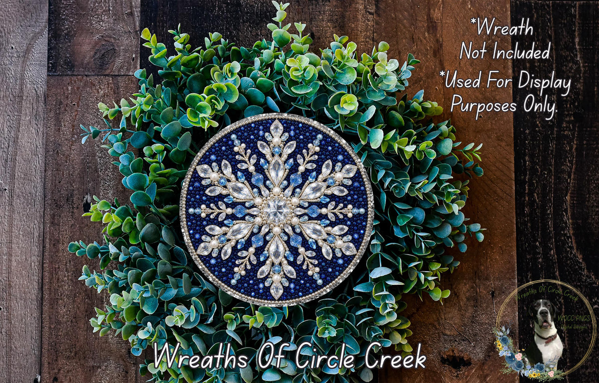 A wreath made of green leaves and a blue and white snowflake-shaped ornament, placed on a wooden surface.