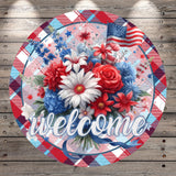 A circular welcome sign featuring a vibrant bouquet of red, white, and blue flowers, along with an American flag, set against a wooden background.