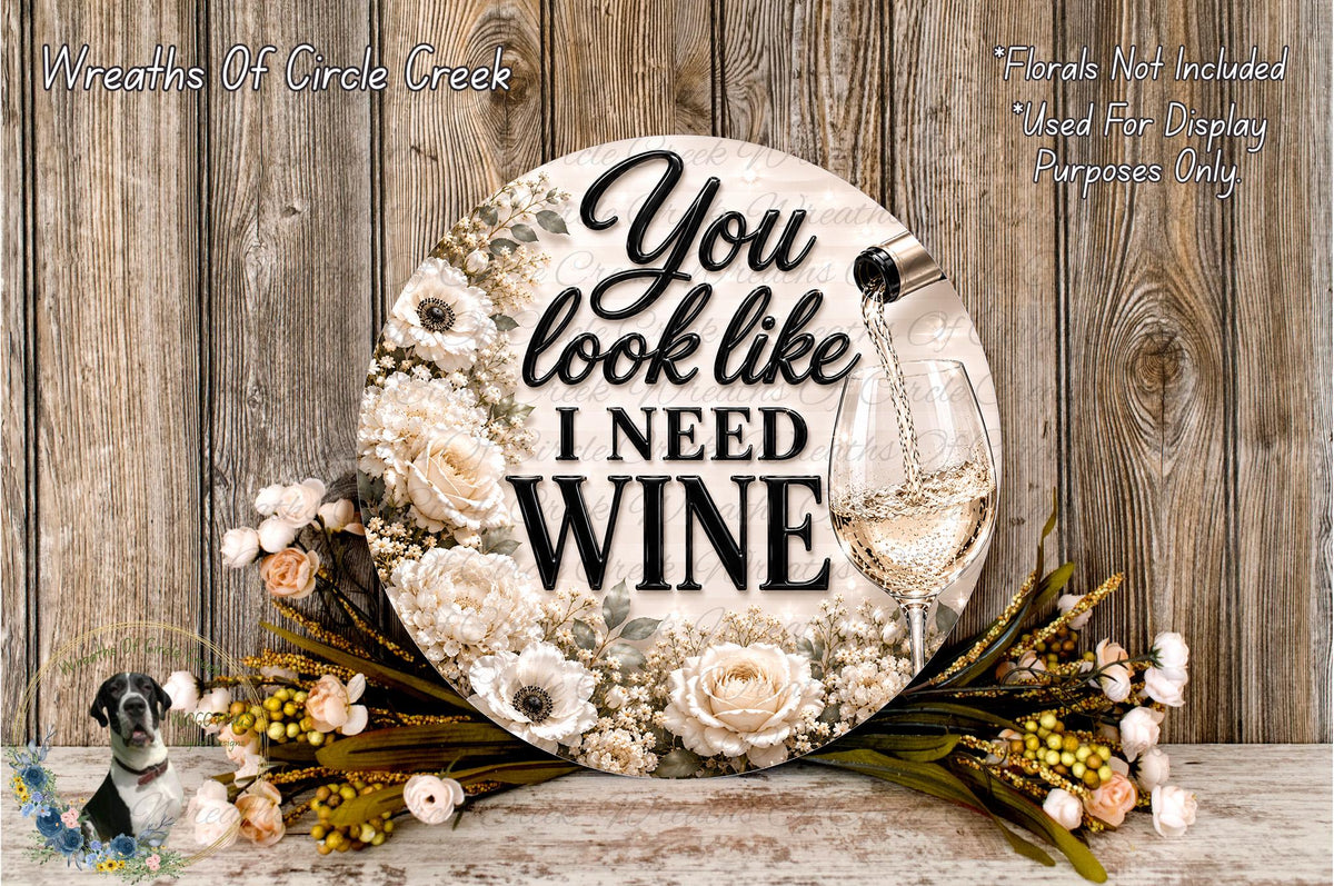 A decorative sign with the text "You look like I need wine" surrounded by a floral arrangement and a wine glass.