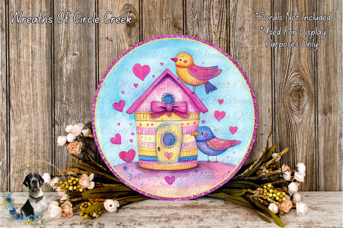 a decorative wreath with a house and birds on it, surrounded by flowers and greenery.