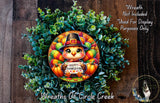 A wreath made of green leaves and colorful autumn-themed elements, including a small turkey wearing a witch's hat and holding a sign that says "Happy Thanksgiving".