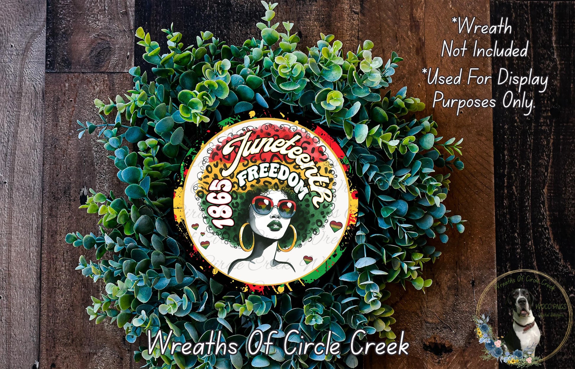 a wreath with a large circular design in the center, surrounded by a lush green plant. The design includes a woman's face with a colorful, vibrant hairstyle and sunglasses. The wreath is displayed on a wooden surface, and there is a small dog visible in the bottom right corner of the image.