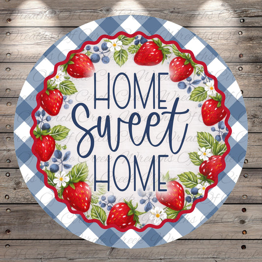 A round sign with a blue and white checkered border, surrounded by a wreath of red strawberries and blueberries. The sign has the text "HOME SWEET HOME" written in a decorative font.