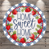 A round sign with a blue and white checkered border, surrounded by a wreath of red strawberries and blueberries. The sign has the text "HOME SWEET HOME" written in a decorative font.