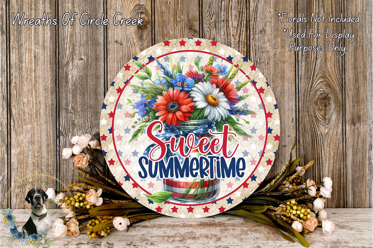 a decorative round sign with a floral arrangement and the text "Sweet Summertime" displayed on it, placed on a wooden surface.