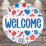 The image is a circular sign with the word "WELCOME" written in bold blue letters. The sign is surrounded by various patriotic symbols, such as stars, hearts, and fireworks, creating a festive and welcoming atmosphere.