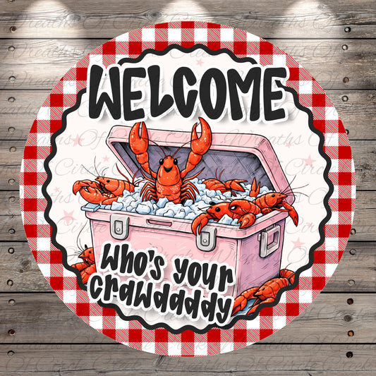 A circular sign with a red and white checkered border, featuring a cartoon illustration of a pink cooler filled with lobsters and the text "Welcome Who's your crawdaddy" in a playful, coastal style.