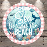 a circular design with a beach scene and a whale, surrounded by a pink and white checkered border.