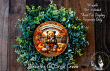 A wreath made of green leaves and a teddy bear, with the text &quot;Welcome To Our Cabin&quot; and a pumpkin and bag of candy.