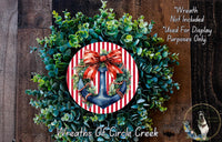 A wreath made of green leaves and a red and white striped anchor, with a red ribbon bow, is displayed on a wooden surface.