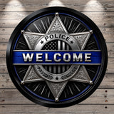 a circular badge with the word "WELCOME" prominently displayed in the center. The badge is surrounded by decorative elements, including stars and stripes, and is set against a wooden background.