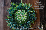 A wreath made of green leaves and a large clover with sparkling jewels, placed on a wooden surface.