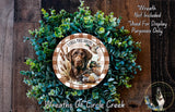 A wreath made of green foliage and featuring a brown dog with a hunting rifle, surrounded by the text "I call the shots" and "Wreaths of Circle Creek".