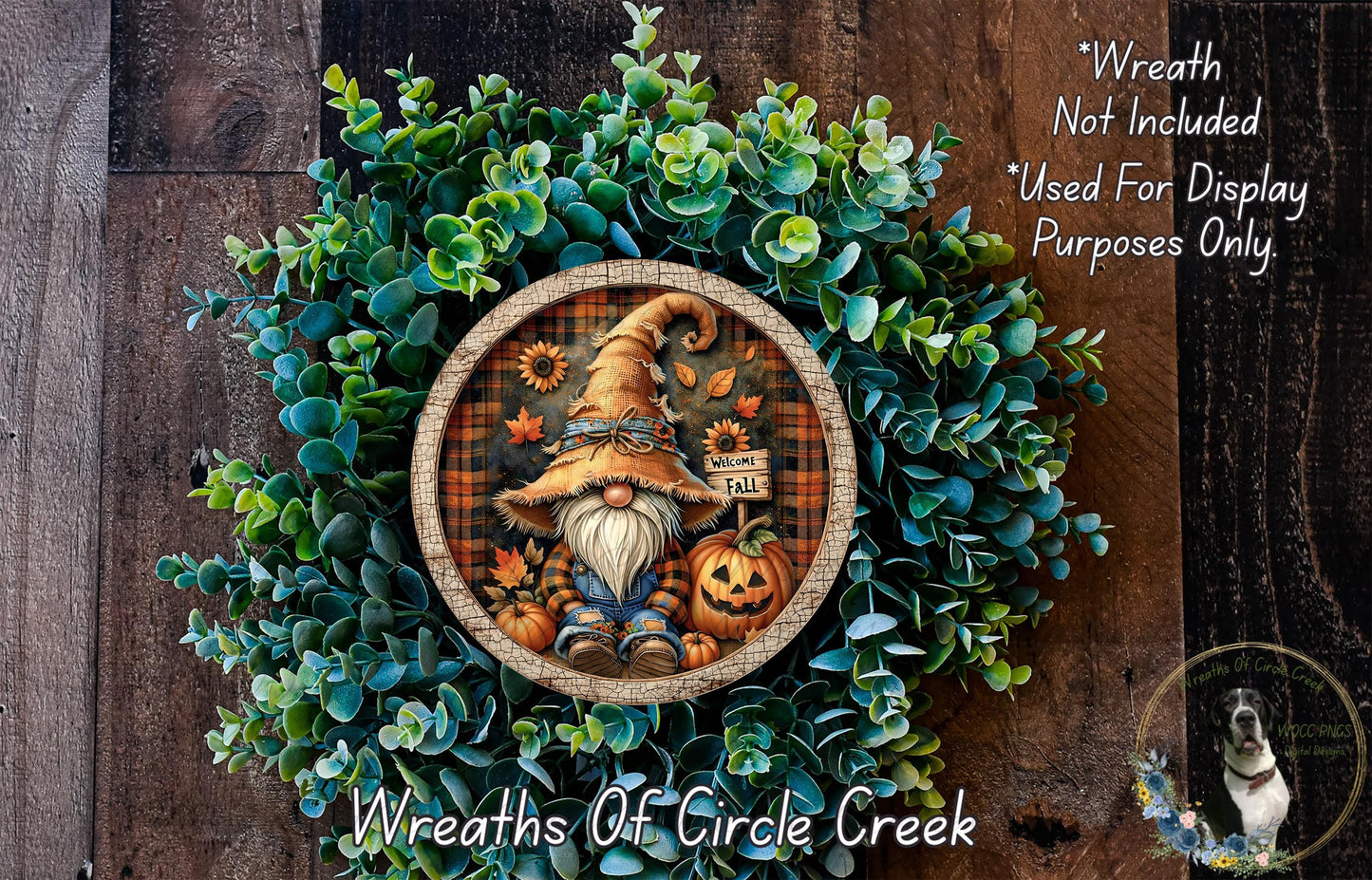 a wreath with a gnome and pumpkins, surrounded by greenery. The wreath is displayed on a wooden surface, and there is a small dog in the bottom right corner.