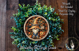 a wreath with a gnome and pumpkins, surrounded by greenery. The wreath is displayed on a wooden surface, and there is a small dog in the bottom right corner.