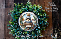 A wreath made of green foliage and pine cones, featuring a small brown squirrel wearing a plaid hat and a "sweater weather" sign.