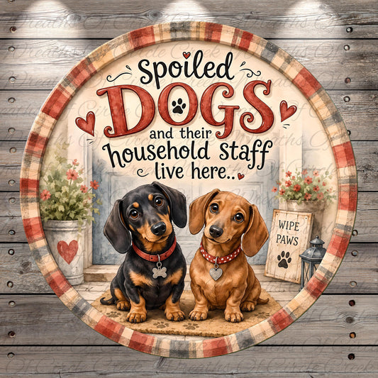 two dogs, one black and one brown, sitting together in front of a house with a sign that says "WIPE PAWS".