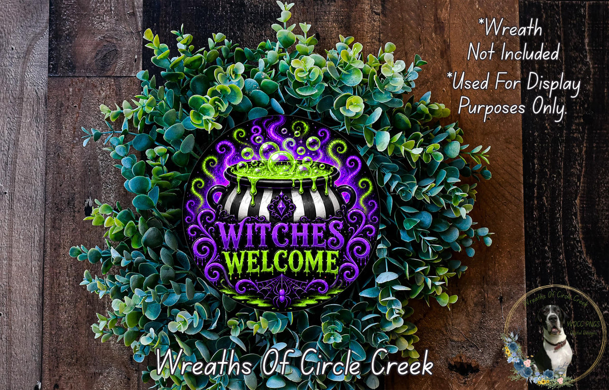 A wreath made of green and purple plants, with a central design featuring the text "WITCHES WELCOME" surrounded by a black and white striped pattern.
