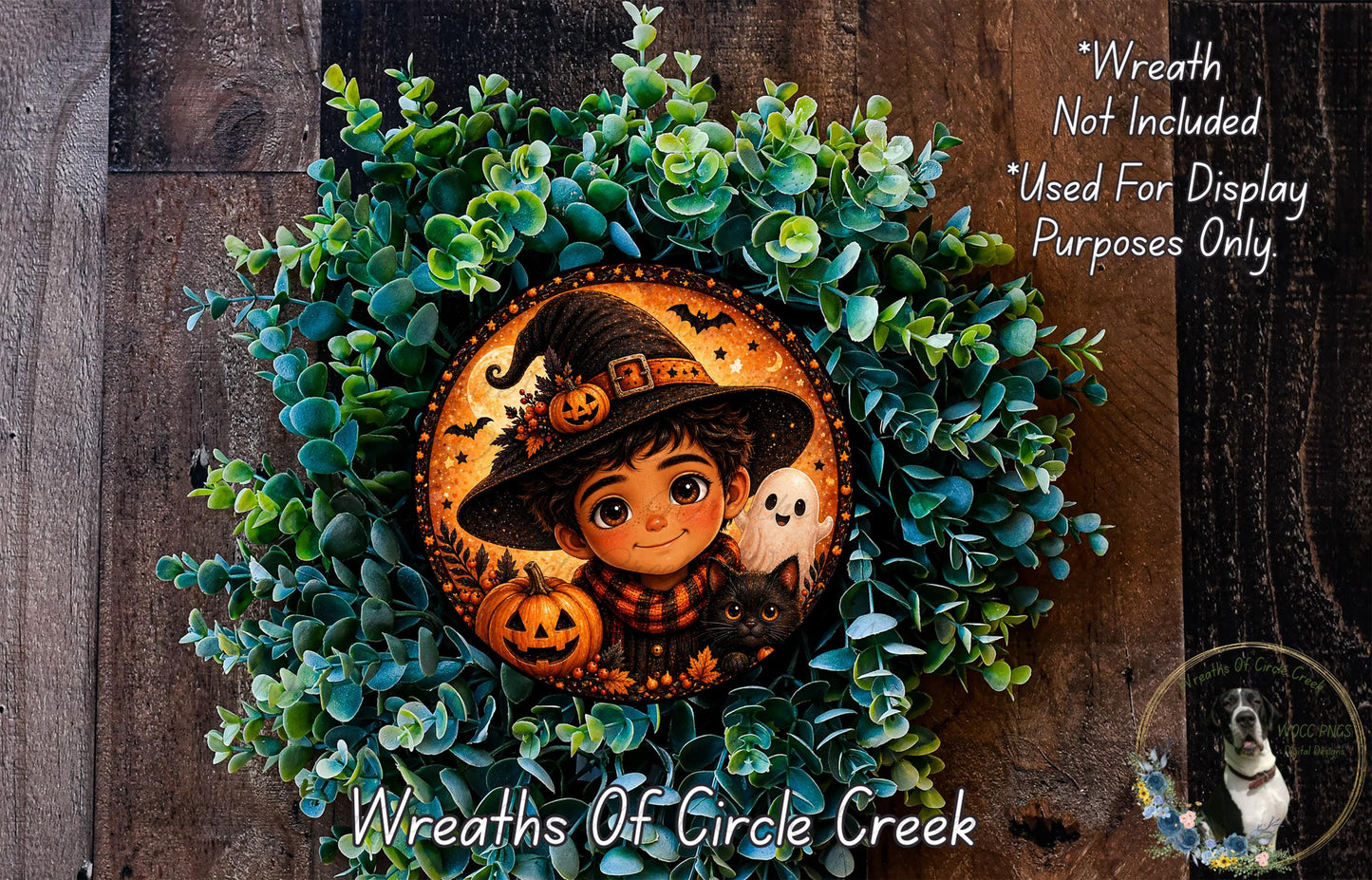 A wreath featuring a young boy wearing a witch's hat, surrounded by green foliage and two carved pumpkins, with a small black cat and a ghost in the background.