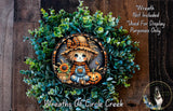 a wreath with a scarecrow and a pumpkin, surrounded by a lush green plant. The wreath is displayed on a wooden surface, and there is a small dog in the bottom right corner of the image.