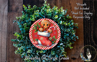 A wreath made of green foliage and a gingerbread man figure, with a red and white striped border, is displayed on a wooden surface.