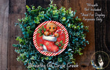 A wreath made of green foliage and a gingerbread man figure, with a red and white striped border, is displayed on a wooden surface.
