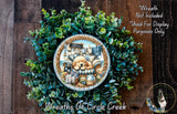 a wreath with a dog and various objects, including a sign that says "Welcome". The wreath is surrounded by a lush green plant, and there is a small dog in the bottom right corner of the image.