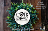 a wreath made of green leaves and a white circular sign with the text "CATS WELCOME HUMANS BY APPOINTMENT ONLY" in the center. The sign is surrounded by a lush wreath, and there is a small dog visible in the bottom right corner of the image.
