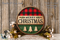 A circular wooden sign with the text "MERRY CHRISTMAS" in the center, surrounded by a plaid pattern and decorated with Christmas trees and flowers.