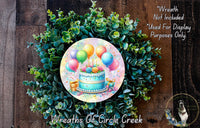 A wreath made of green leaves and colorful balloons, with a birthday cake and presents on top, is displayed on a wooden surface.