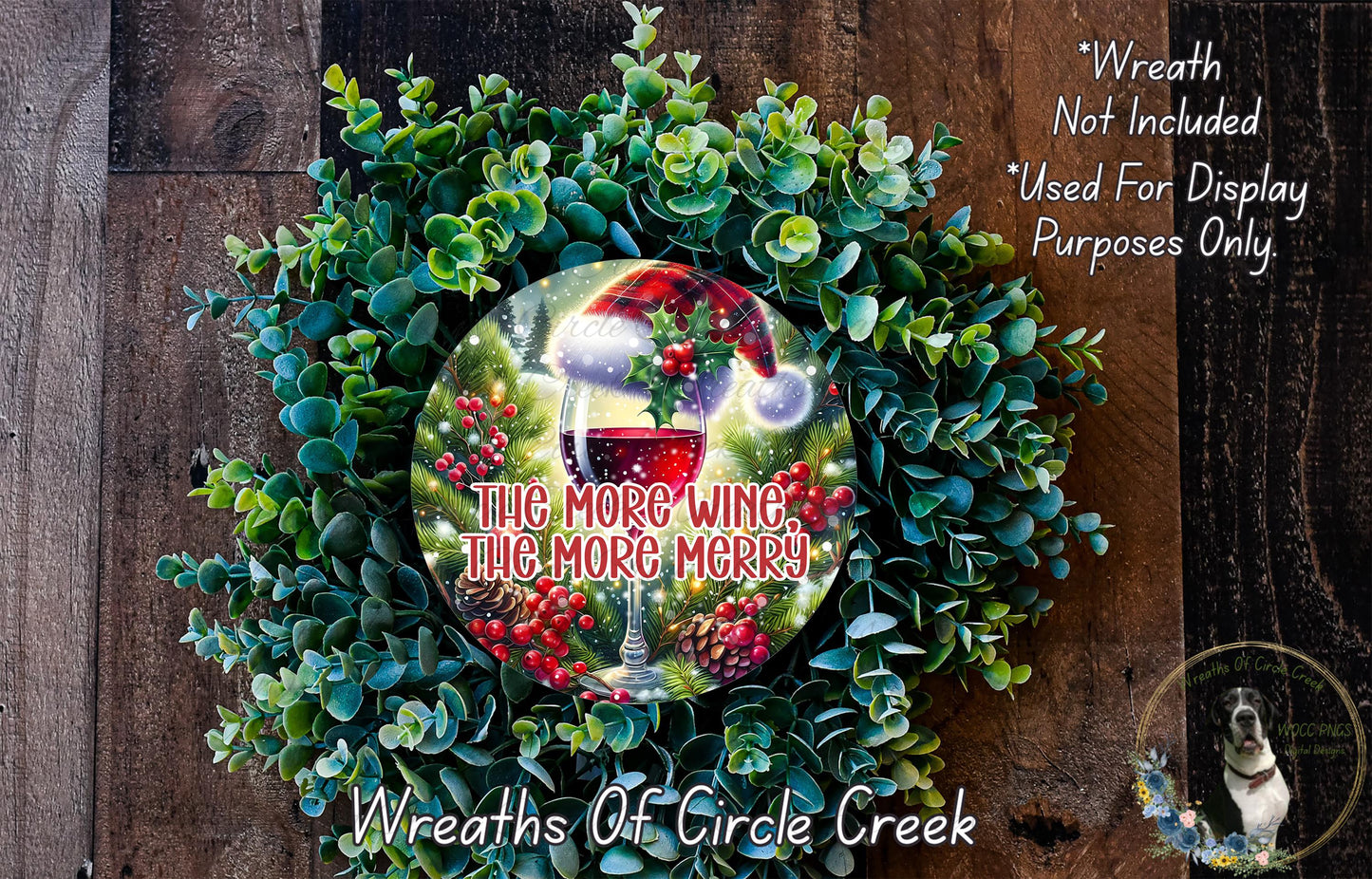 A wreath made of evergreen branches and berries, with a wine glass and a red ribbon in the center. The wreath is displayed on a wooden surface, and there is a text overlay that reads "The more wine, the merrier!" and "Wreaths of Circle Creek".