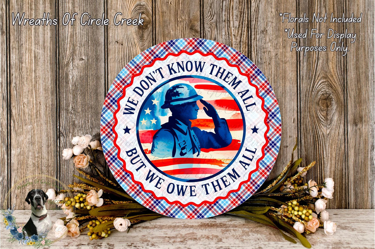 A patriotic wreath with a soldier saluting, surrounded by flowers and a wooden background.