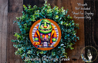 A wreath featuring a cartoon character with a green body, orange and purple accents, and a pumpkin, surrounded by a lush green plant.