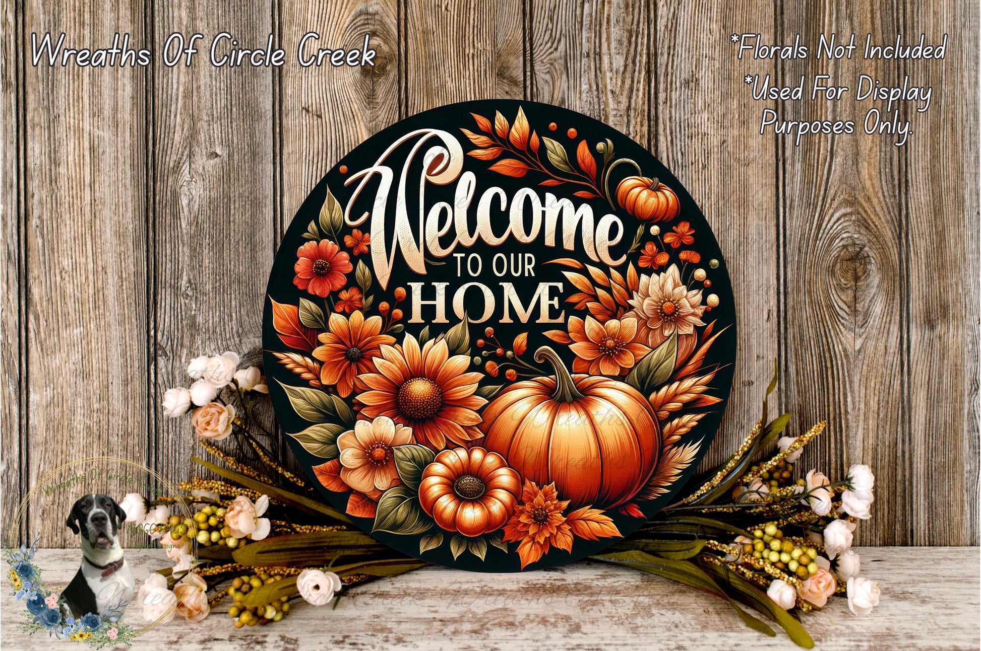 a decorative sign with the text "Welcome to our Home" surrounded by a vibrant arrangement of autumn flowers, including pumpkins, sunflowers, and other seasonal elements. The sign is displayed on a wooden surface, and there are additional floral arrangements in the background.