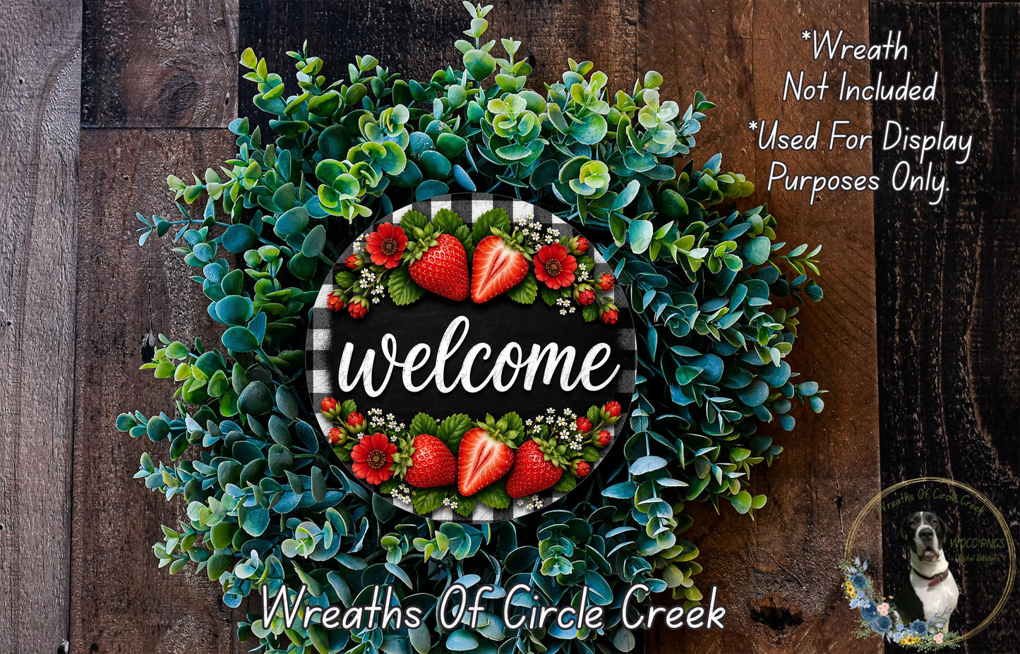 a wreath with a welcome sign in the center, surrounded by various green and red flowers, including strawberries. The wreath is displayed on a wooden surface, and there is a small dog in the bottom right corner of the image.