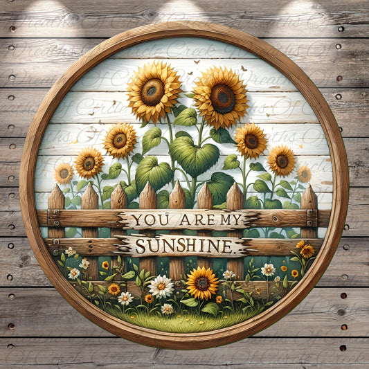 A circular wooden frame with a painted scene of a sunflower garden, featuring a wooden fence with the text "You are my sunshine" written on it.