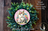A wreath made of green plants and flowers, with a white rabbit wearing a flower crown and holding a sign that says "Easter".