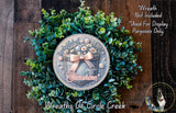 A wreath made of green leaves and flowers, with a circular design featuring a ribbon and the text "Sunshine" in the center.