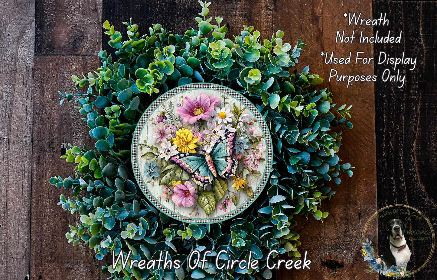 A wreath made of various green plants and flowers, including a butterfly, is displayed on a wooden surface.