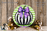 a decorative pumpkin with a purple bow, surrounded by flowers and placed on a wooden surface.