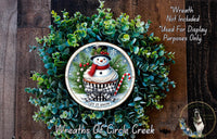 A wreath made of green foliage and a snowman decoration, with the text "Let it snow" on the snowman.
