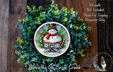 A wreath made of green foliage and a snowman decoration, with the text "Let it snow" on the snowman.